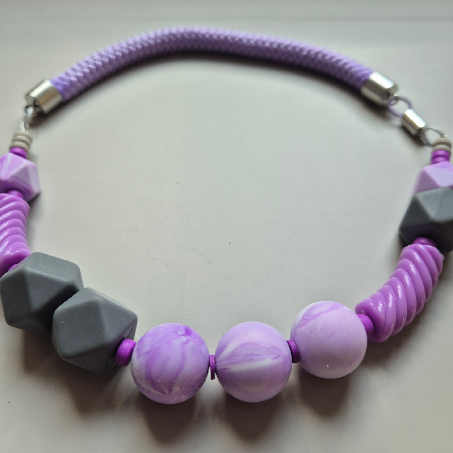 Necklace of grey geometric beads, lavender marbled spheres and purple discs on a lilac braided rope