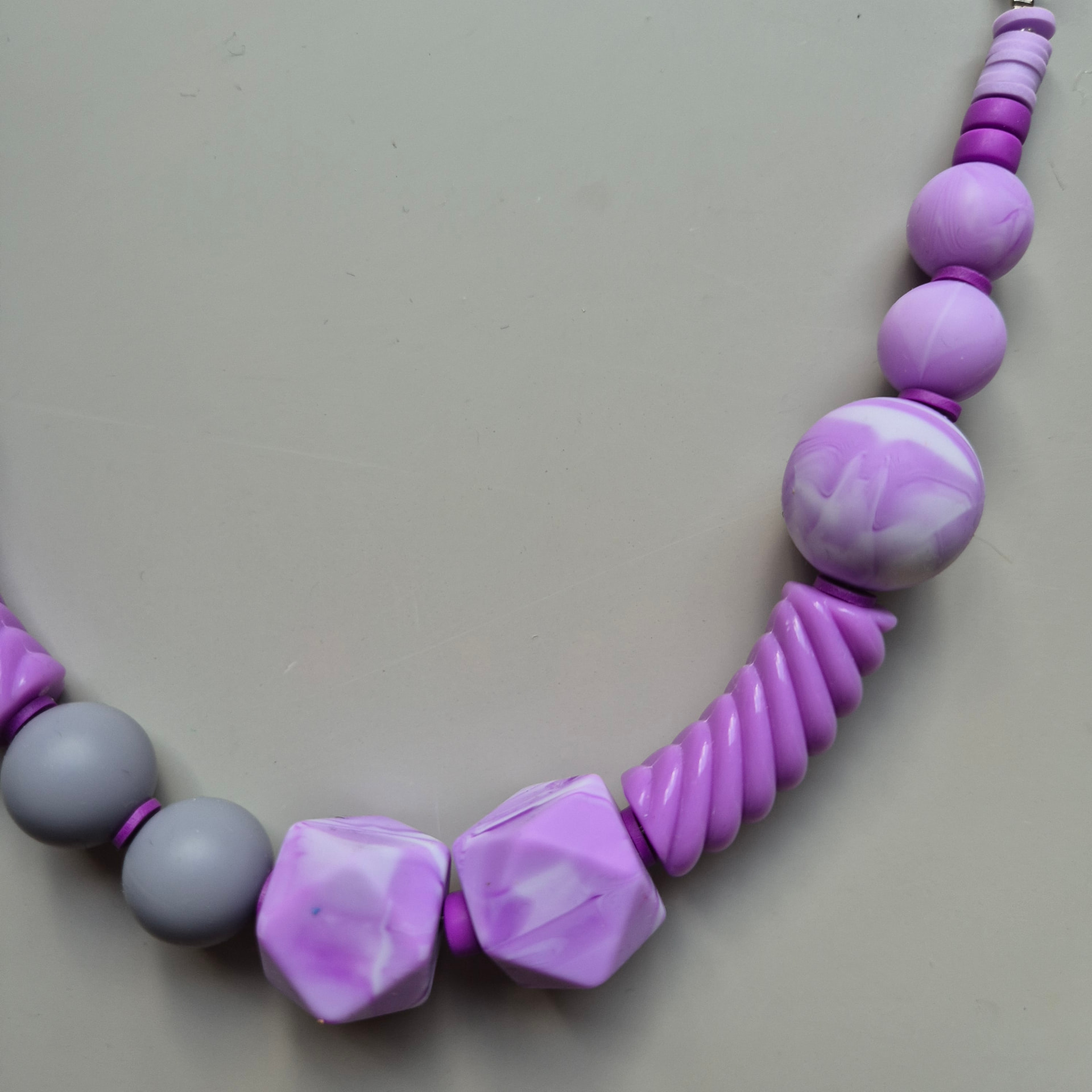 Close view of Secret with lilac marbled spheres, lilac facets and spiral tubes on a grey braided rope