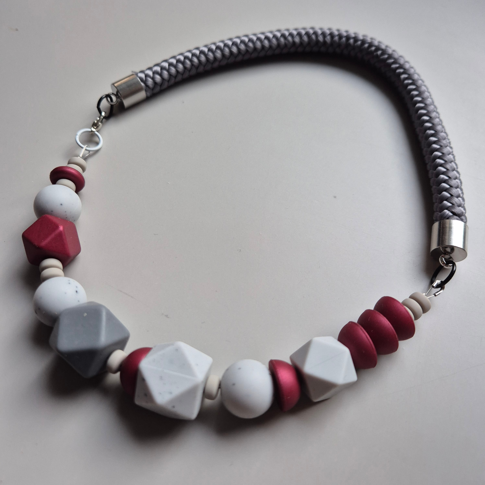 Necklace of white speckled faceted beads and burgundy metallic discs on a grey braided rope
