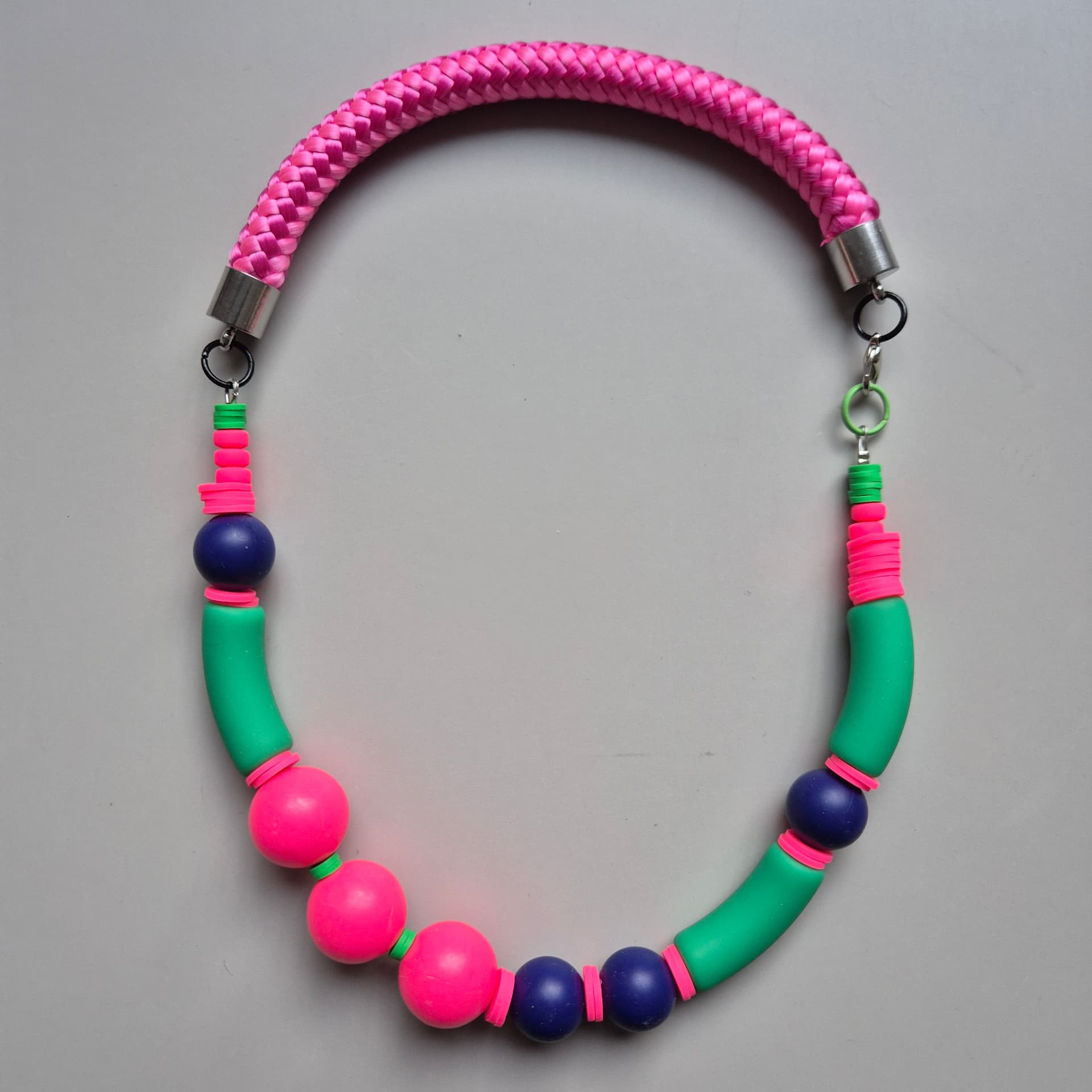Flat-lay of a neon pink, green and navy beaded necklace on braided pink rope