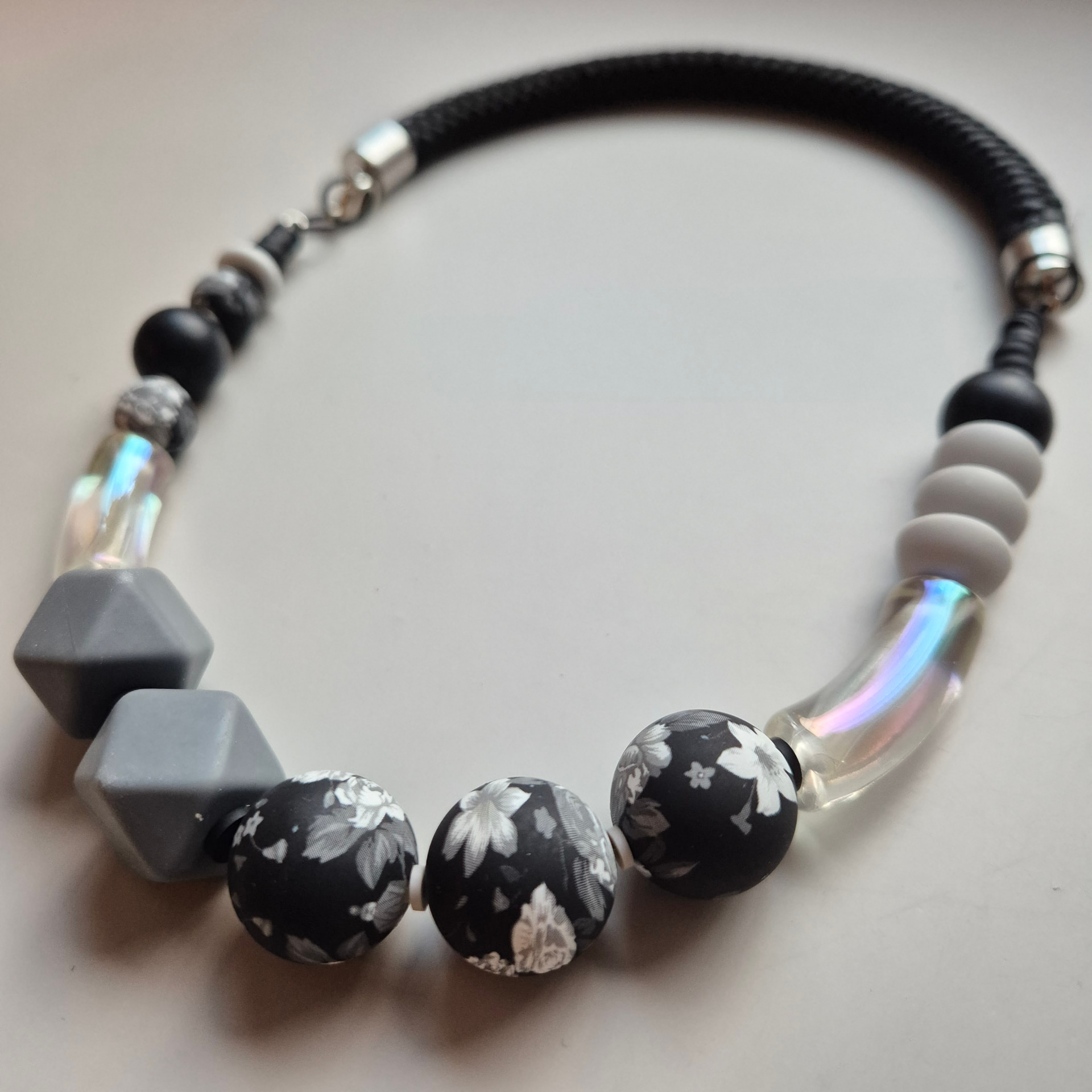 Black-and-white necklace with grey geometric beads, floral spheres and iridescent tubes on a black rope