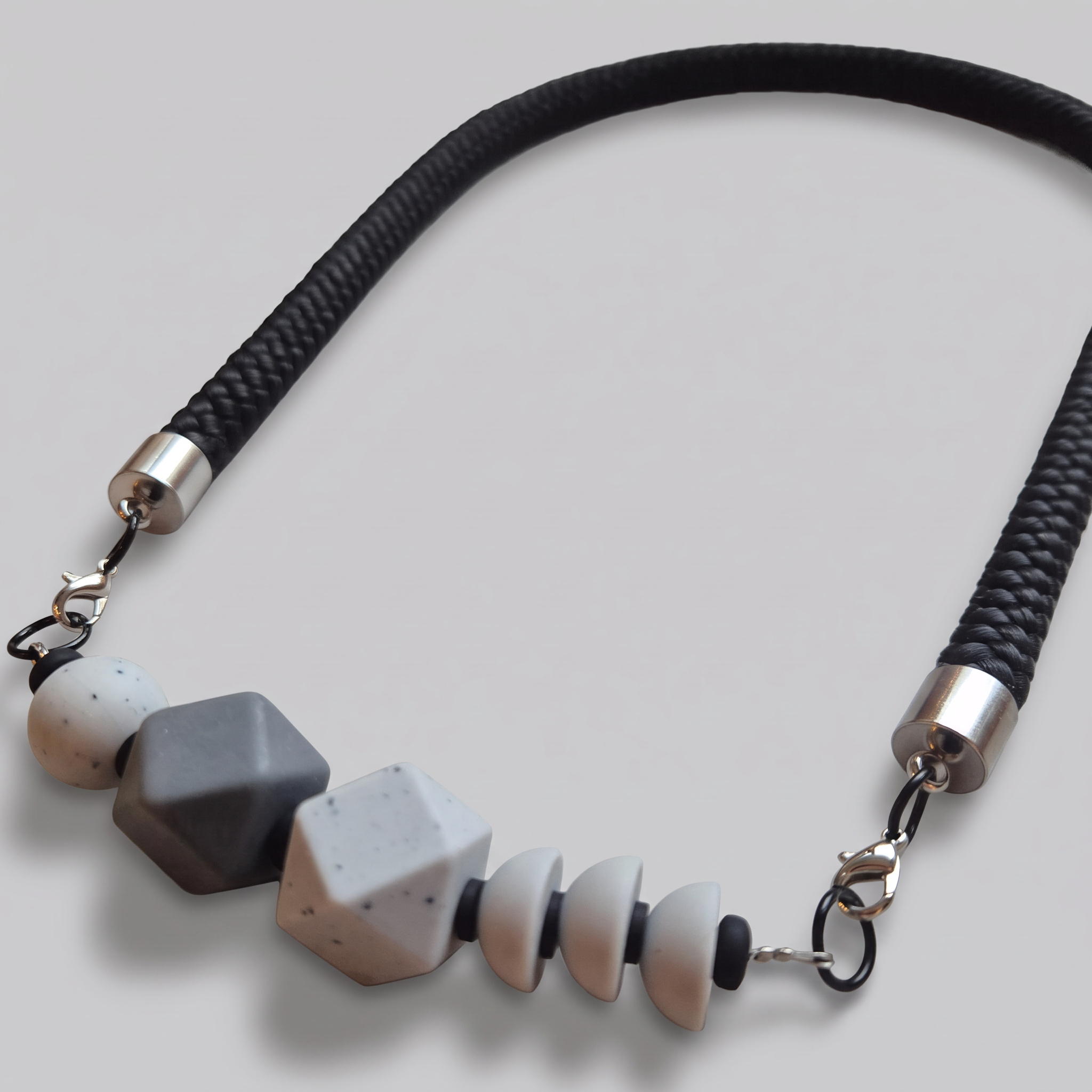 Necklace with a grey geometric bead, speckled grey faceted beads and grey discs on a black rope