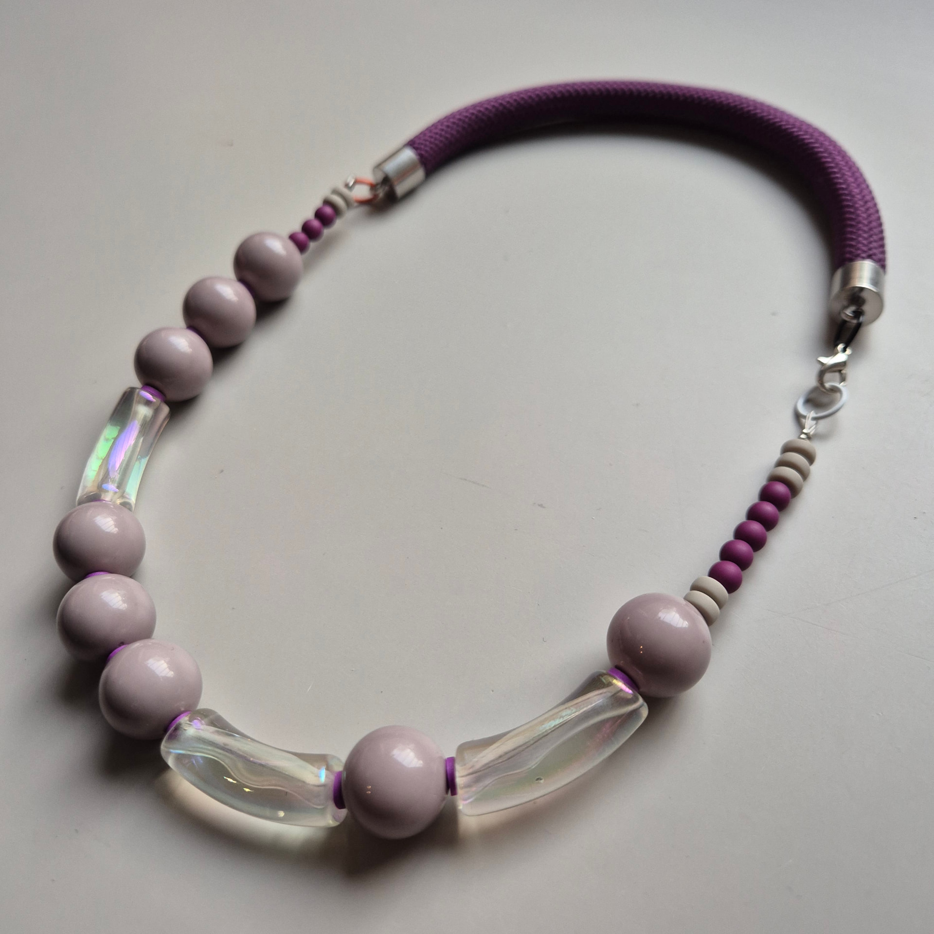 Necklace of mauve ceramic spheres and iridescent clear glass tubes on a plum rope