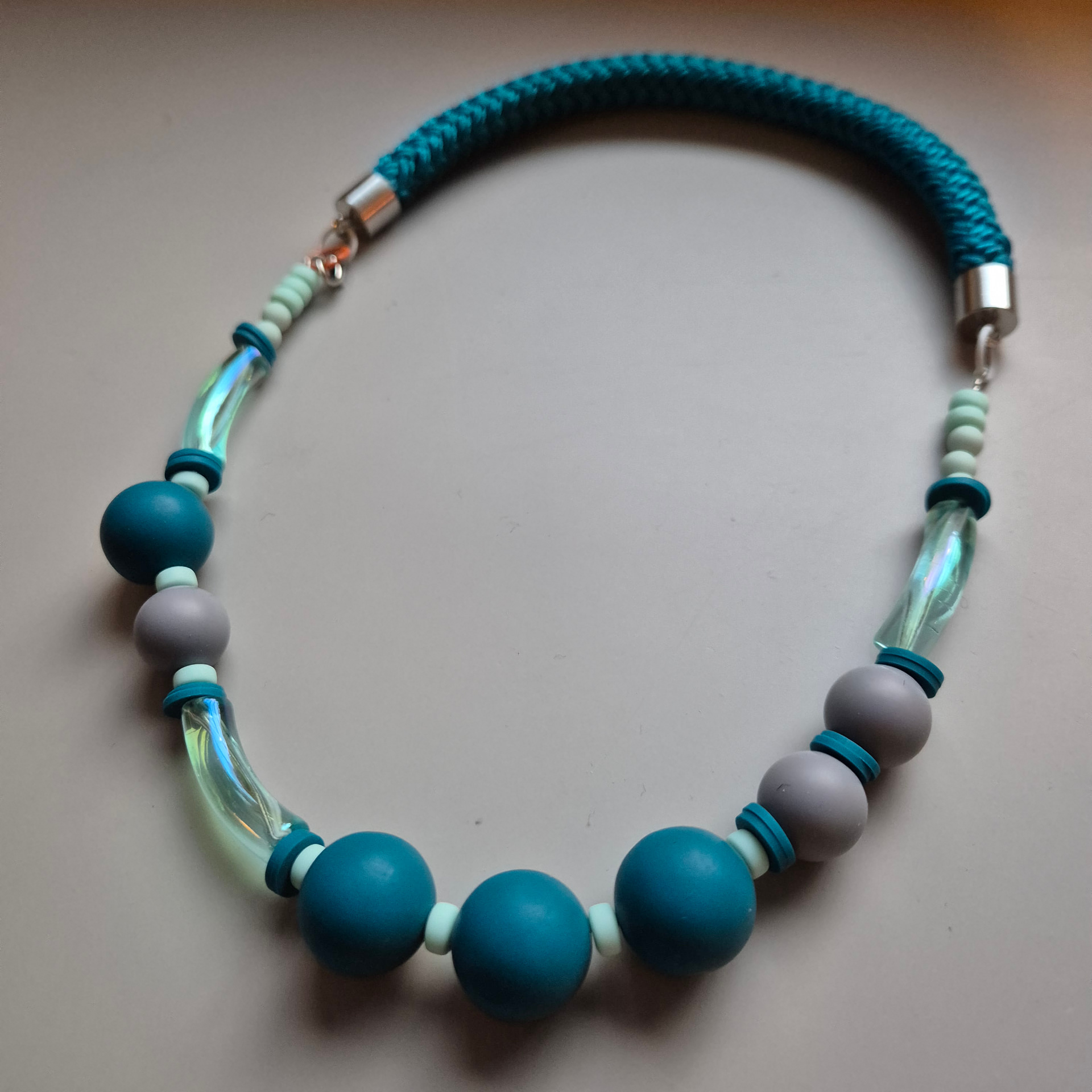 Necklace of teal wooden spheres, grey beads and iridescent glass tubes on a teal braided rope