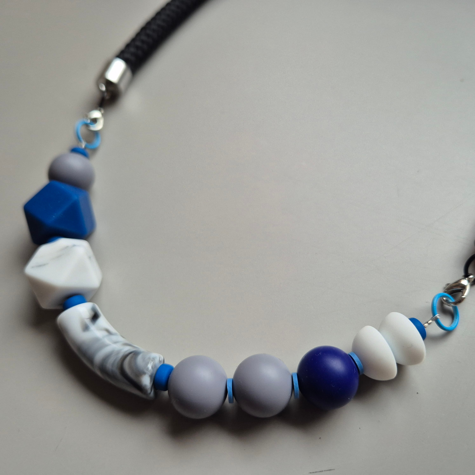 Necklace with grey and blue spheres, white and marbled geometric beads, white discs and blue rings on a black rope