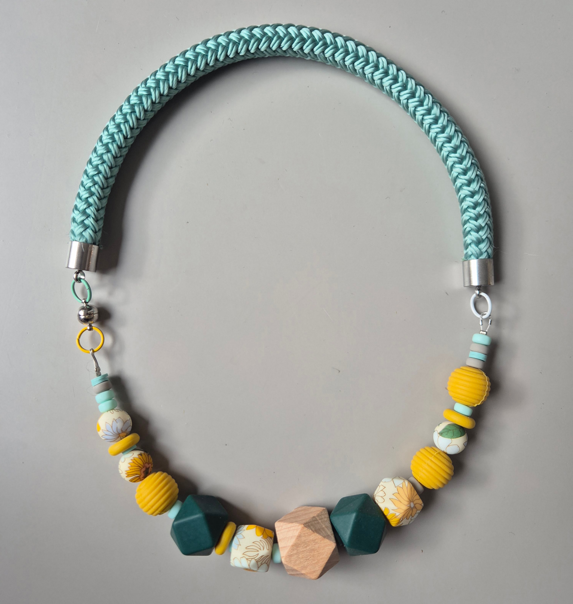 Necklace with teal braided rope, yellow tubes, floral silicone beads, wood geometric bead and grey facets