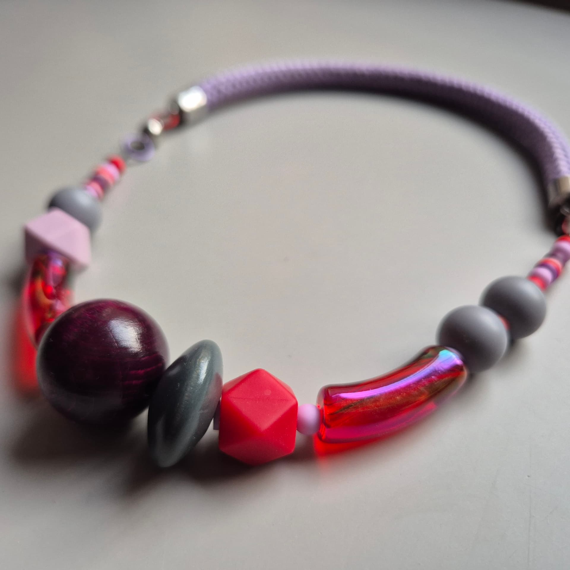 Necklace with a deep plum wooden sphere, red faceted bead and iridescent red glass tube on a lilac rope