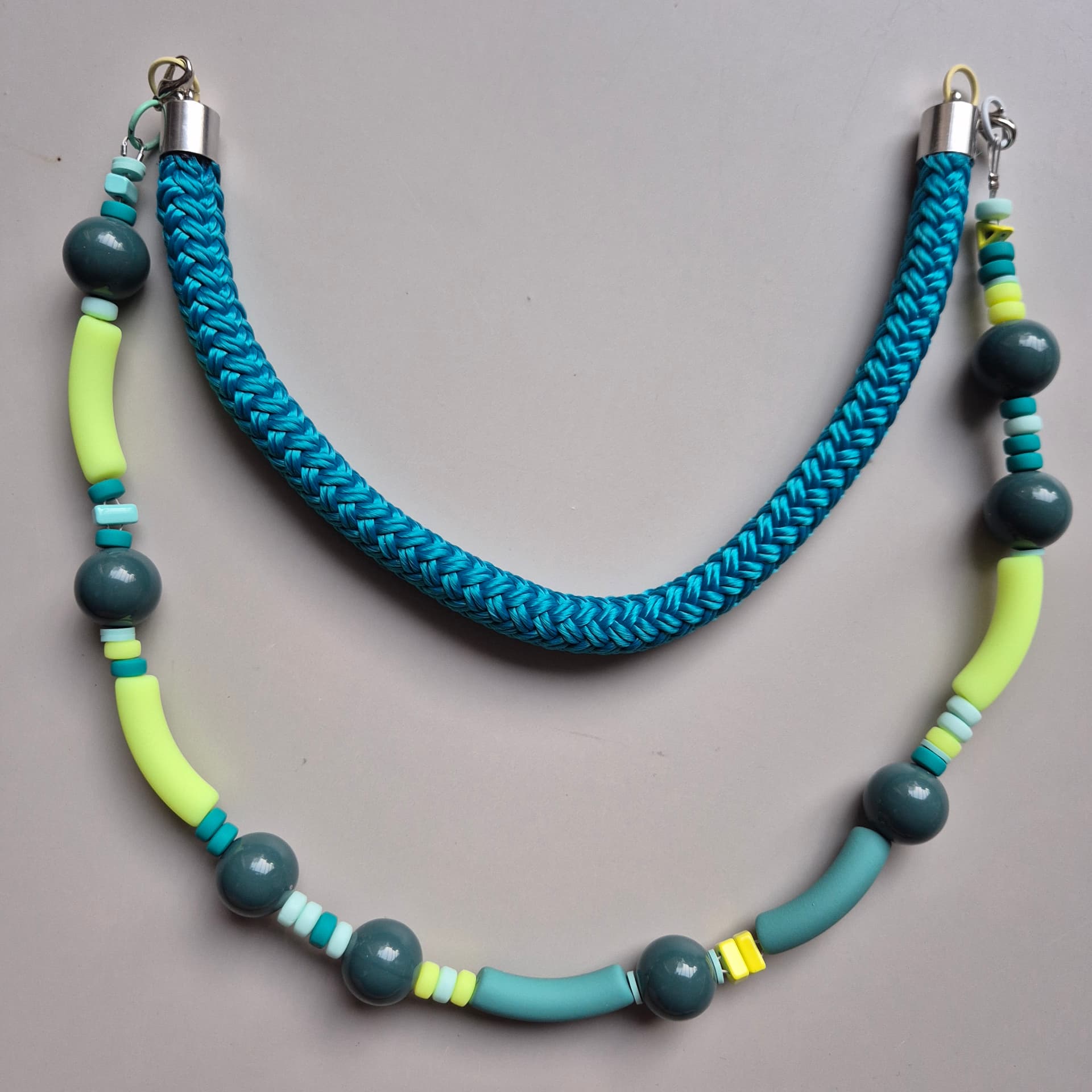 Two-strand necklace with teal ceramic spheres, neon yellow curved tubes and a braided blue rope