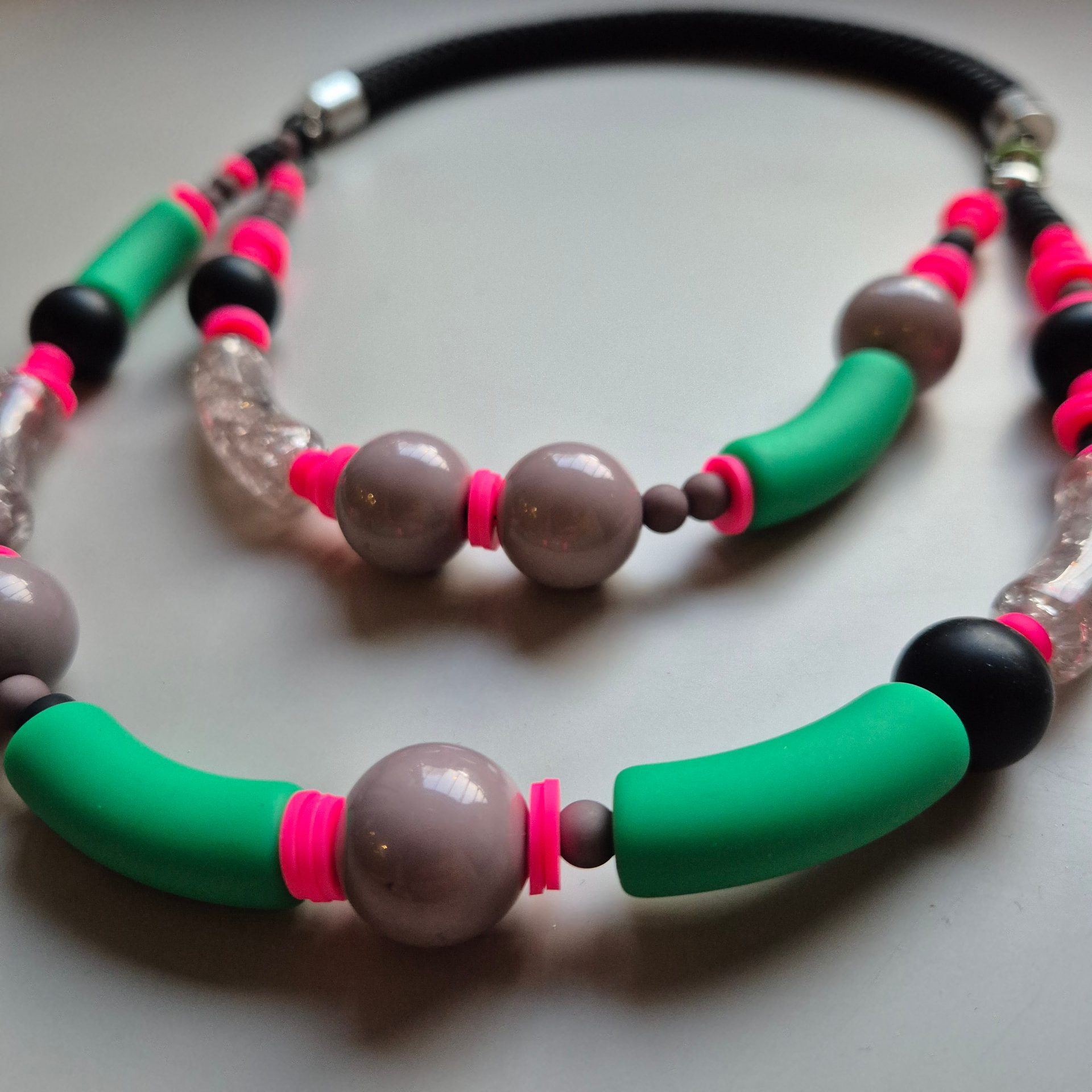 Necklace with green silicone tubes, neon pink discs, mauve spheres and crackled clear glass on a black rope