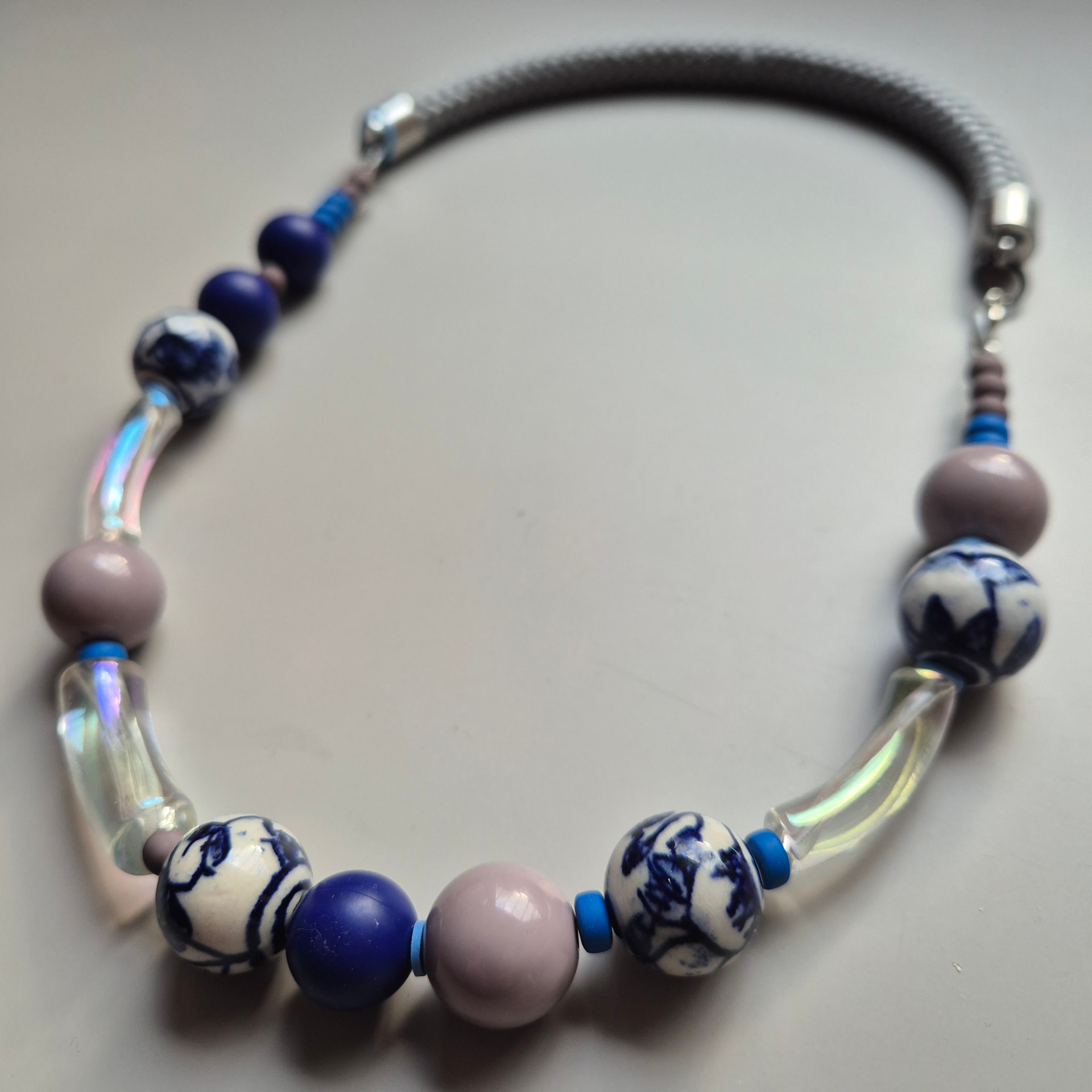 Necklace with Delft blue and white porcelain beads, iridescent curved tubes, navy spheres and grey beads on a grey rope