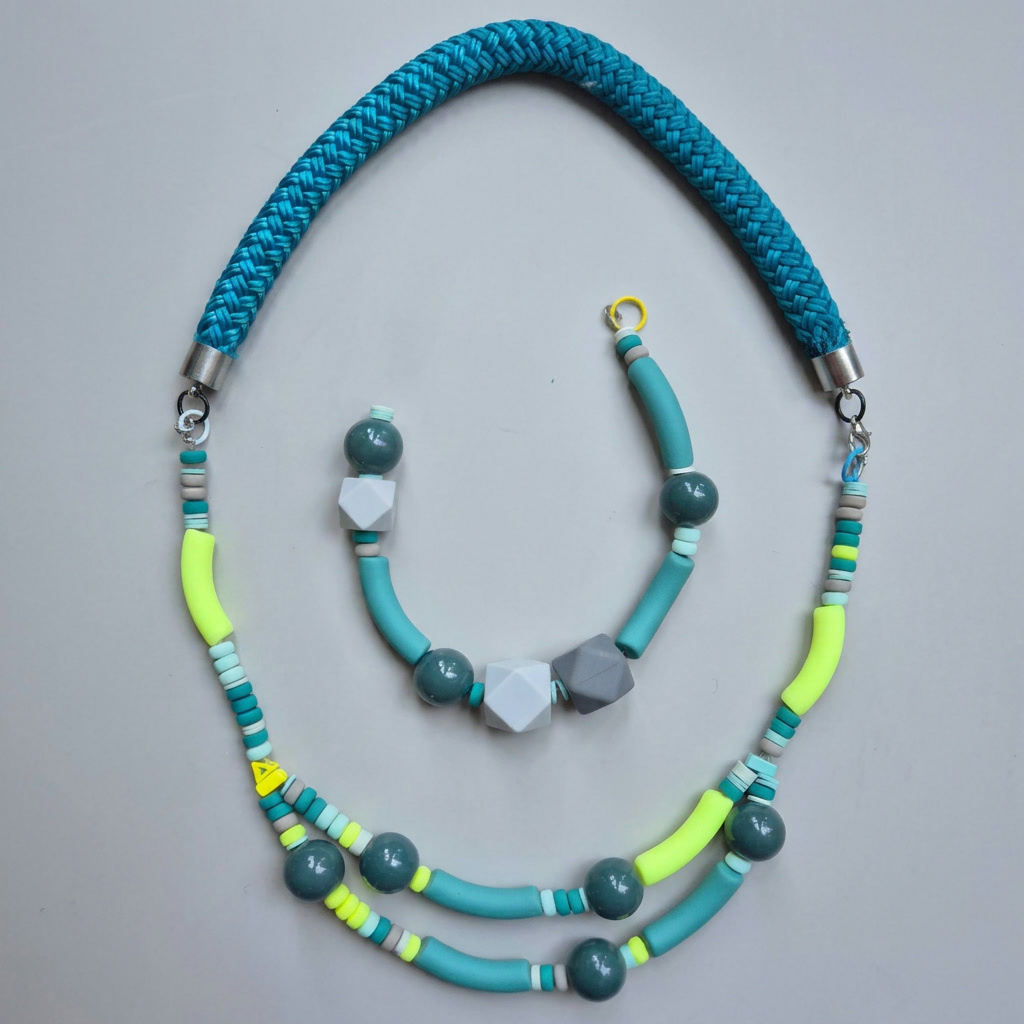 Multi-strand teal necklace with yellow tubes, teal beads and grey geometric facets on a braided blue rope