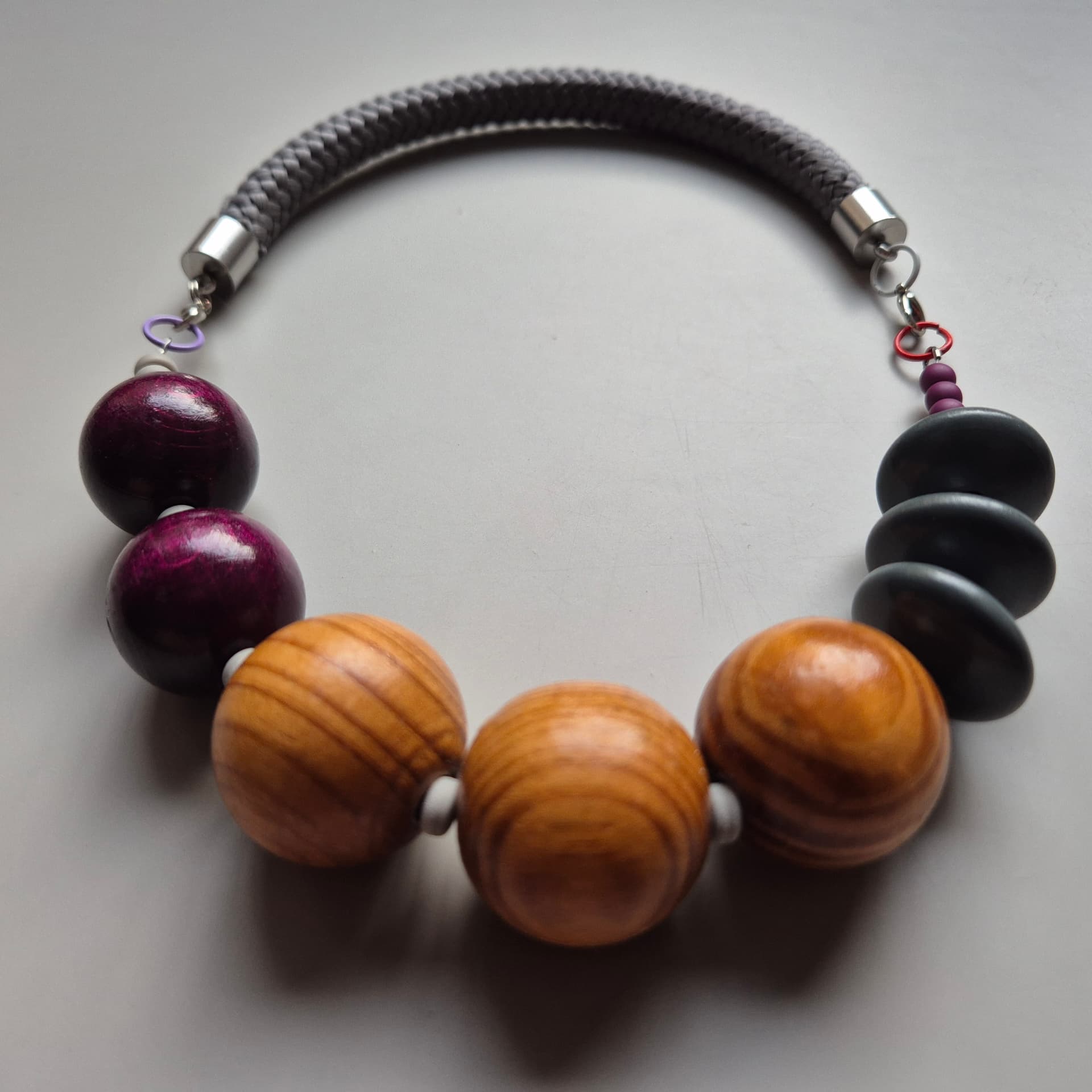 Necklace of olive wood spheres, plum stained wood and matte black discs on a grey rope