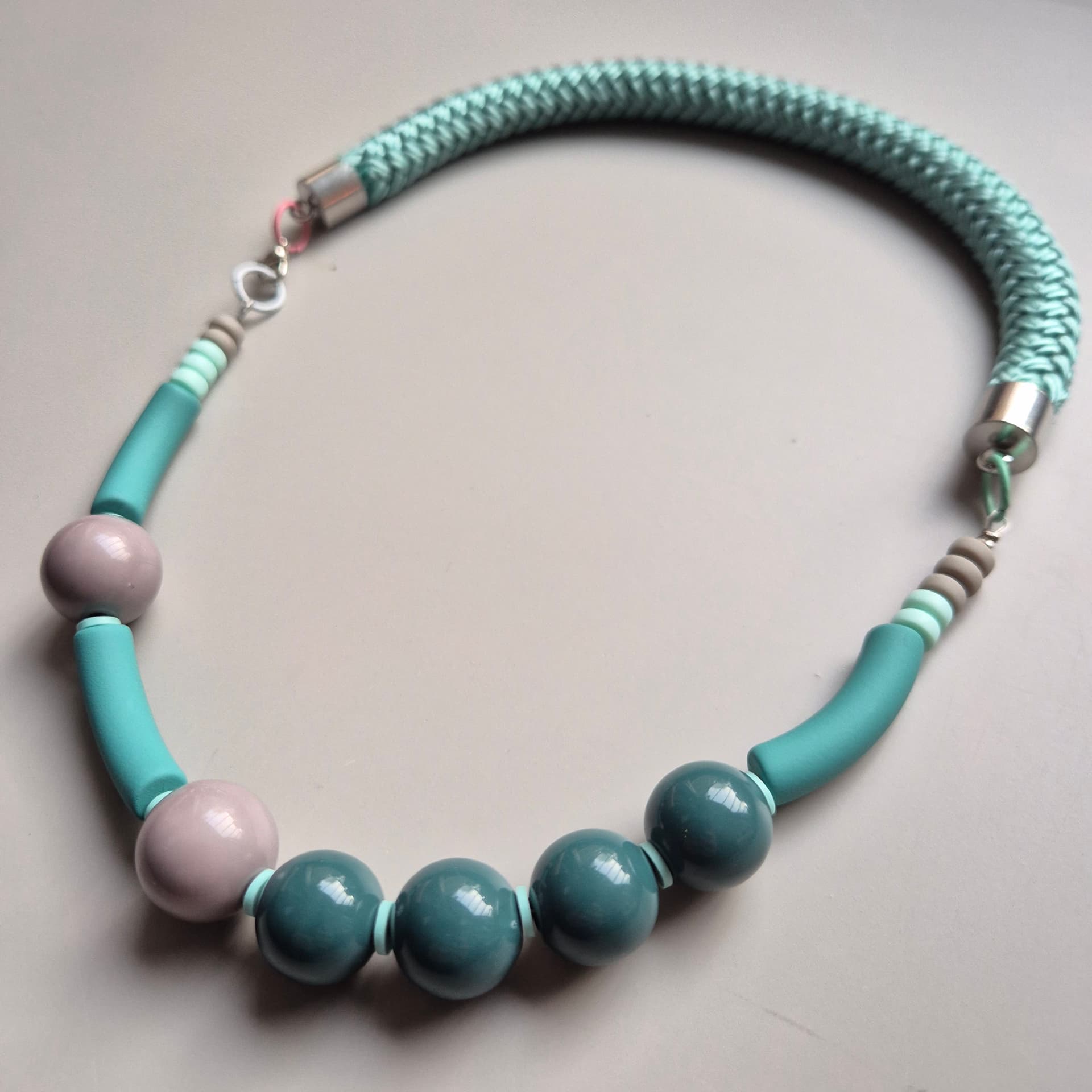 Necklace of glossy teal ceramic spheres and dusty rose beads on a mint braided rope