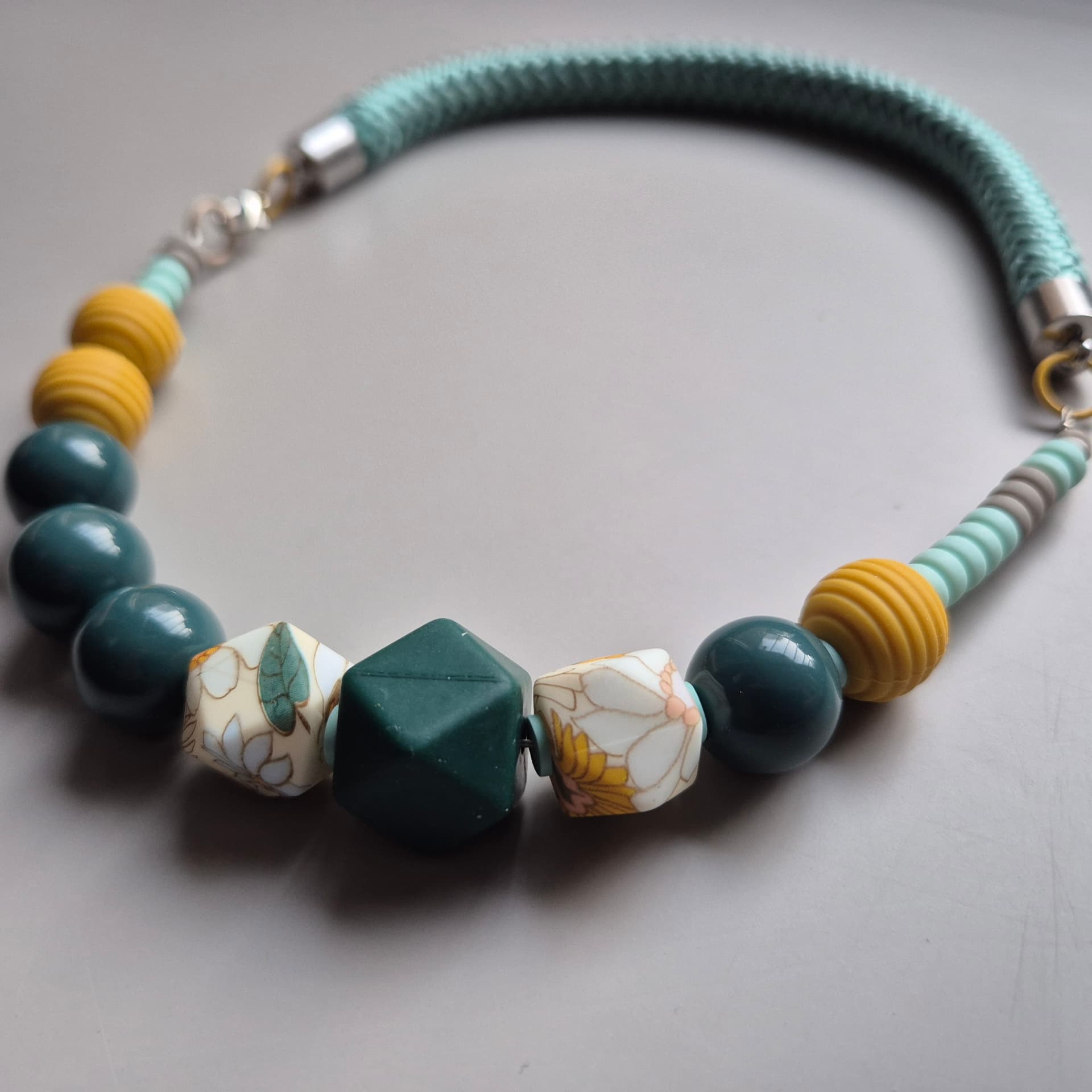 Necklace with floral porcelain facets, ochre ribbed beads and deep teal spheres on teal rope