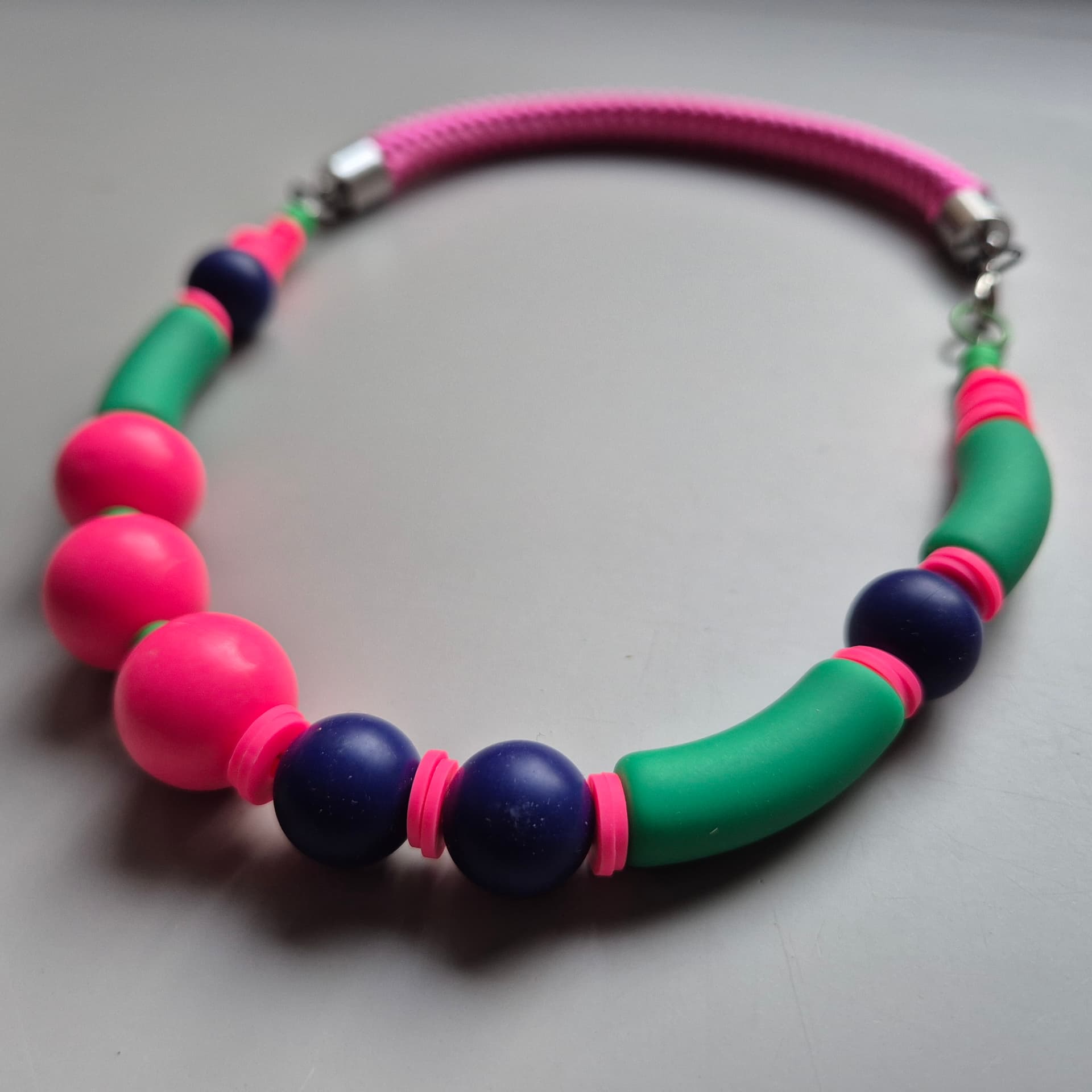 Necklace with neon pink spheres, green curved tubes and navy beads on a pink rope